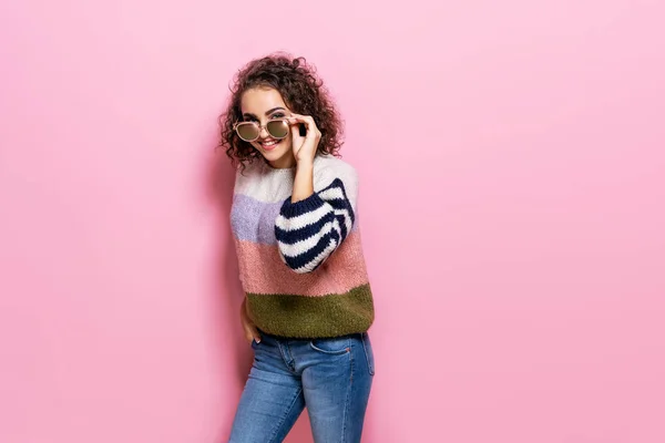 Menina bonita com cabelo encaracolado posando em suéter elegante no fundo pastel rosa . — Fotografia de Stock