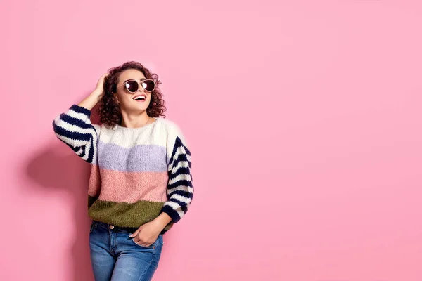 Menina bonita feliz com incrível sorriso de dente posando em camisola elegante, jeans e óculos de sol no fundo pastel rosa . — Fotografia de Stock