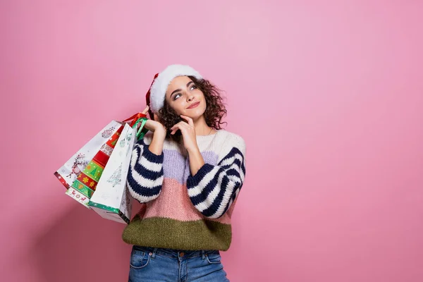 Hermosas mujeres vistiendo brillante Navidad llevando coloridas bolsas de compras. Sobre fondo rosa. Compras de Navidad y feliz año nuevo . — Foto de Stock