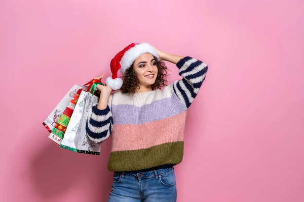 Hermosas mujeres vistiendo brillante Navidad llevando coloridas bolsas de compras. Sobre fondo rosa. Compras de Navidad y feliz año nuevo . — Foto de Stock