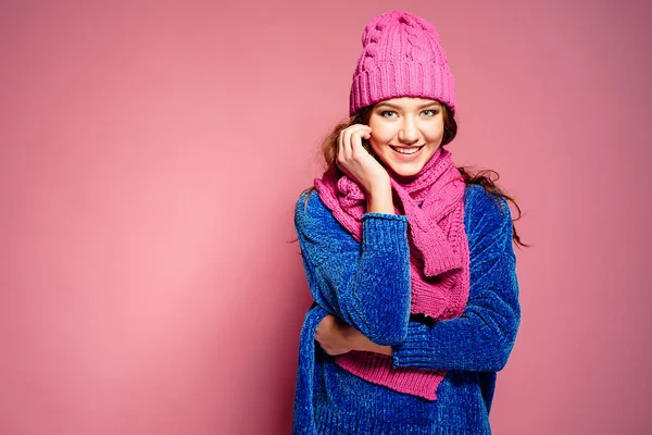 Modern ung kvinna klädd i blå tröja och rosa mössa och halsduk poserar, gör roliga ansiktsuttryck. — Stockfoto