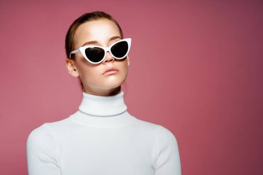 Muhteşem zarif kadın beyaz örme golf ve pembe duvardan poz güneş gözlüğü.