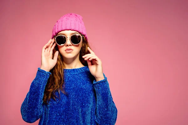 Moderní mladá žena na sobě modrý svetr a růžový klobouk lodě, dělat legrační výraz obličeje. — Stock fotografie