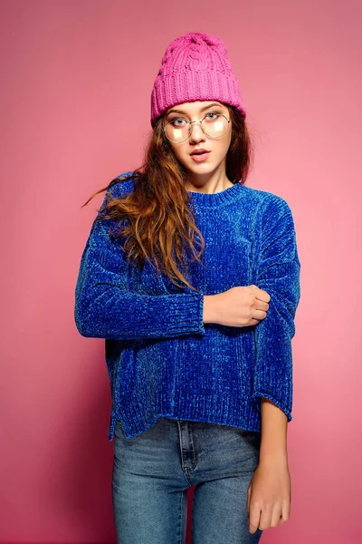 Mujer joven y moderna con suéter azul y sombrero rosa posando, haciendo expresión facial divertida . —  Fotos de Stock