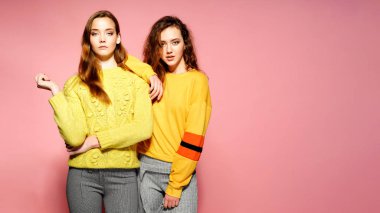 Kameraya bakarak iki güzel seksi gülümseyen güzel kızlar. Kazak, pembe bir arka plan üzerinde sıcak kadın şık duran sarı.