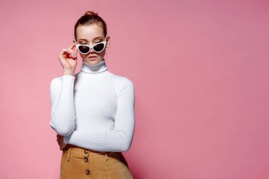 Muhteşem zarif kadın beyaz örme golf ve pembe duvardan poz güneş gözlüğü.