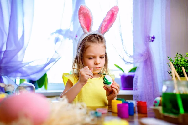 Щаслива великодня дівчина у вухах кролика малює яйця, маленька дитина вдома. весняне свято — стокове фото