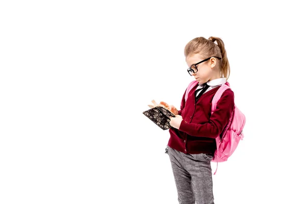 Παιδί με τσάντας. Κορίτσι με λευκό πουκάμισο και γκρι παντελόνι, στρογγυλεμένες γυαλιά, κρατήστε ένα βιβλίο, σχολική τσάντα και ποζάρει σαν μοντέλο δείχνει δάχτυλο επάνω. Απομονωμένα σε λευκό — Φωτογραφία Αρχείου