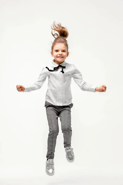 Hermosa niña en camisa blanca y pantalones grises de pie cerca de la pared blanca y posando como modelo — Foto de Stock