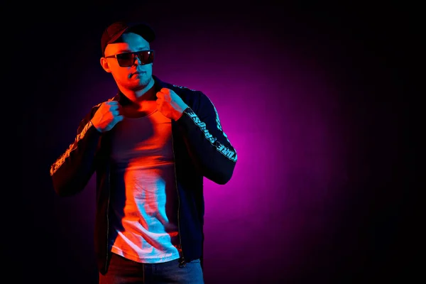 Portrait of a young happy serious man at studio. High Fashion male model in colorful bright neon lights posing on black background. — Stock Photo, Image