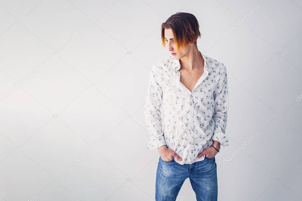 Fashion portrait of young man in white shirt poses over grey wall