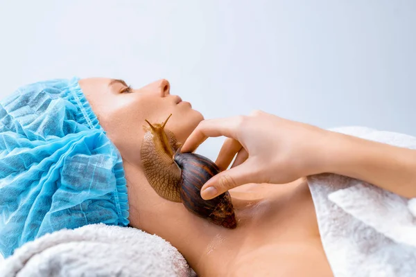 Mladá žena podstupující léčbu s obří šneky Oblovka v salonu krásy — Stock fotografie