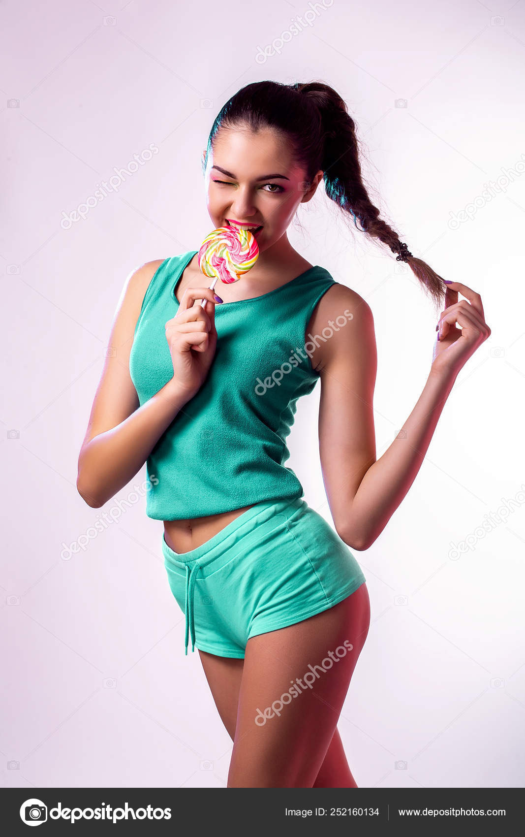 Funny young girl in green jumpsuit holding lollipop and posing for camera  onwhite background. Stock Photo by ©zamuruev 252160134