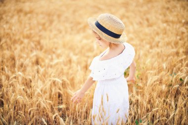 Mutlu çocuk sonbahar buğday alanında. Güzel kız beyaz elbise ve hasır şapka iyi eğlenceler oynarken, hasat