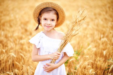 Mutlu çocuk sonbahar buğday alanında. Güzel kız beyaz elbise ve hasır şapka iyi eğlenceler oynarken, hasat