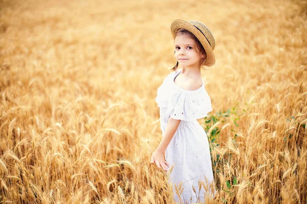 Gelukkig kind in herfst tarweveld. Mooi meisje in een witte jurk en stro hoed veel plezier met spelen, oogsten — Stockfoto