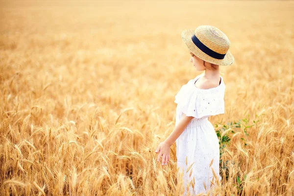 Glückliches Kind im Herbstweizenfeld. schöne Mädchen in weißem Kleid und Strohhut haben Spaß beim Spielen, Ernten — Stockfoto