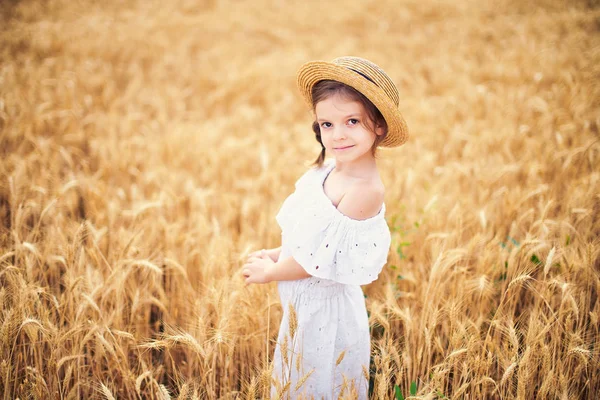 Happy child in autumn wheat field. Beautiful girl in white dress and straw hat have fun with playing, harvesting — Stock Photo, Image