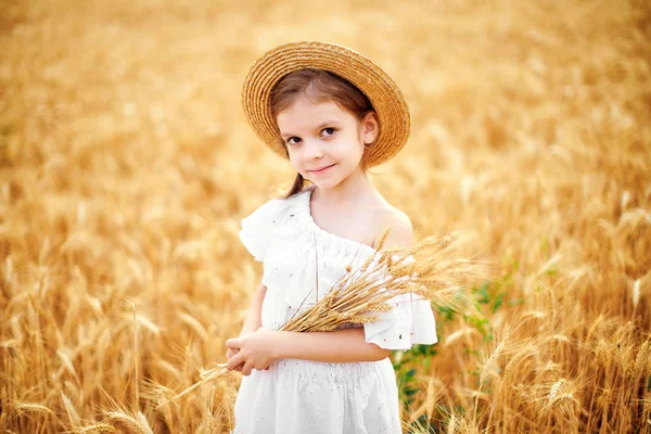 Szczęśliwe dziecko w jesień pole pszenicy. Piękna dziewczyna w białej sukni i słomkowy kapelusz do zabawy z gry, maszyny do zbioru — Zdjęcie stockowe
