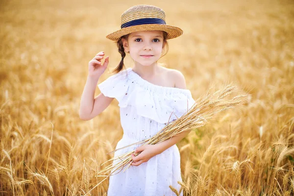 Criança feliz no campo de trigo de outono. Menina bonita em vestido branco e chapéu de palha se divertir com o jogo, colheita — Fotografia de Stock