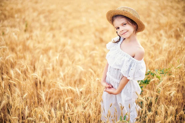 Šťastné dítě v podzimní pšeničné pole. Krásná dívka v bílých šatech a slaměný klobouk bavit s hraním, sklizeň — Stock fotografie