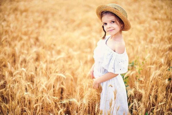 Boldog gyermek őszi búza mezőben. A szép lány a fehér ruha és szalmakalap szórakozni játszik, szüret — Stock Fotó