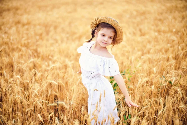 Gelukkig kind in herfst tarweveld. Mooi meisje in een witte jurk en stro hoed veel plezier met spelen, oogsten — Stockfoto