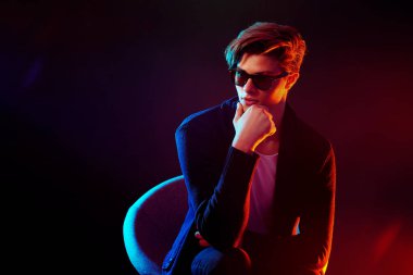 Siyah ceket ve güneş gözlüğü serin şık adam. Yüksek moda erkek modeli siyah arka plan üzerine poz renkli parlak neon ışıkları. Sanat tasarım konsepti