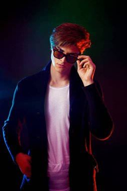 Siyah ceket ve güneş gözlüğü serin şık adam. Yüksek moda erkek modeli siyah arka plan üzerine poz renkli parlak neon ışıkları. Sanat tasarım konsepti