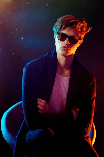 Cool stylish man in black jacket and sunglasses. High Fashion male model in colorful bright neon lights posing on black background. Art design concept — Stock Photo, Image