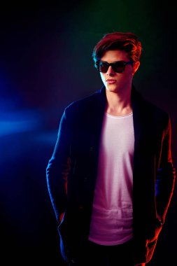 Siyah ceket ve güneş gözlüğü serin şık adam. Yüksek moda erkek modeli siyah arka plan üzerine poz renkli parlak neon ışıkları. Sanat tasarım konsepti