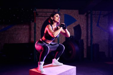 Çekici uygun orta yaş kadın bir CrossFit tarzında kutu atlama yapıyor. Kadın atlet spor salonunda atlar performans