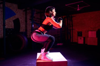 Çekici uygun orta yaş kadın bir CrossFit tarzında kutu atlama yapıyor. Kadın atlet spor salonunda atlar performans