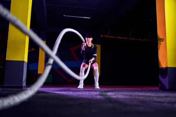 Mujer fitness usando cuerdas de entrenamiento para hacer ejercicio en el gimnasio. Atleta haciendo ejercicio con cuerdas de batalla en el gimnasio cruzado —  Fotos de Stock