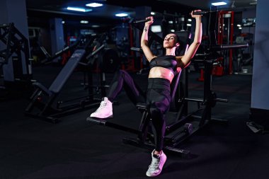 Spor salonunda egzersiz yapan atletik seksi kadın - yan görüş - makine kullanarak