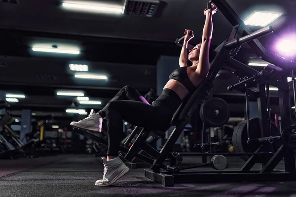 Atletische sexy vrouw doen oefening met behulp van machine in sportschool - zijaanzicht — Stockfoto