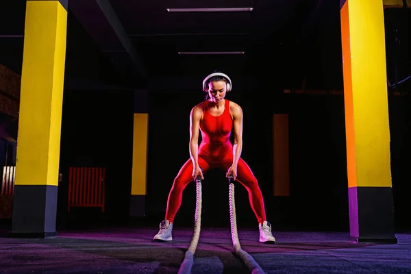 Mujer fitness usando cuerdas de entrenamiento para hacer ejercicio en el gimnasio. Atleta haciendo ejercicio con cuerdas de batalla en el gimnasio cruzado — Foto de Stock