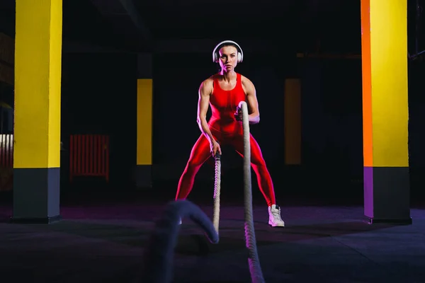Mujer fitness usando cuerdas de entrenamiento para hacer ejercicio en el gimnasio. Atleta haciendo ejercicio con cuerdas de batalla en el gimnasio cruzado —  Fotos de Stock