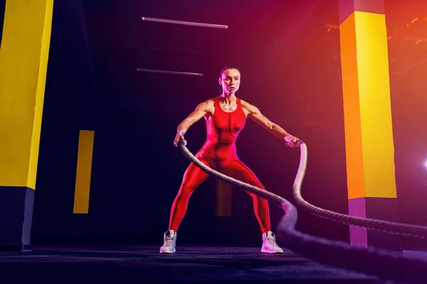 Mujer fitness usando cuerdas de entrenamiento para hacer ejercicio en el gimnasio. Atleta haciendo ejercicio con cuerdas de batalla en el gimnasio — Foto de Stock