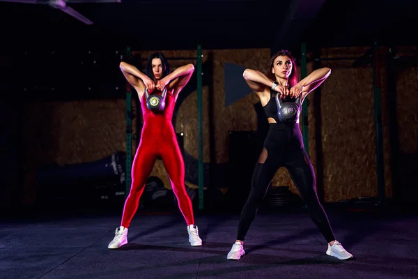 Dos mujeres atletas atractivas en forma realizando un swing de timbre en el gimnasio — Foto de Stock