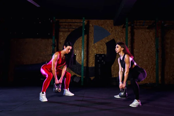 Dos mujeres atletas atractivas en forma realizando un swing de timbre en el gimnasio — Foto de Stock