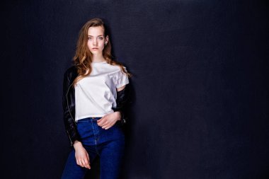 Beyaz tişörtlü ve siyah deri ceketli genç bir kadın. Siyah stüdyo arka planı. İzole edilmiş