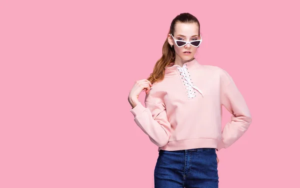 Молодая красивая женщина в розовом свитере и солнцезащитных очках изолированы на розовом фоне студии — стоковое фото
