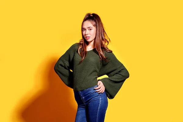 Retrato de uma bela jovem mulher em casual sorrindo e olhando por cima do ombro enquanto posando no fundo do estúdio amarelo. — Fotografia de Stock