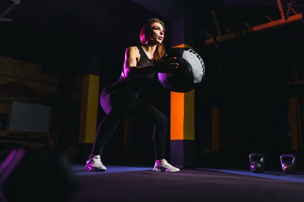 Спортсменка виконує присідання з фітнес-кулькою. Жіночі вправи і розтягування з медичним м'ячем у спортзалі — стокове фото