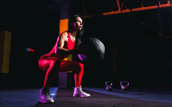 Deportiva haciendo ejercicios de sentadilla con pelota de fitness. Ejercicio femenino y estiramiento con balón de medicina en el gimnasio — Foto de Stock