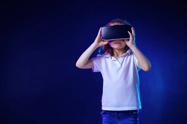 Menina 7 anos. experimentando jogo de fone de ouvido VR em fundo colorido. Criança usando um gadget de jogo para realidade virtual . — Fotografia de Stock