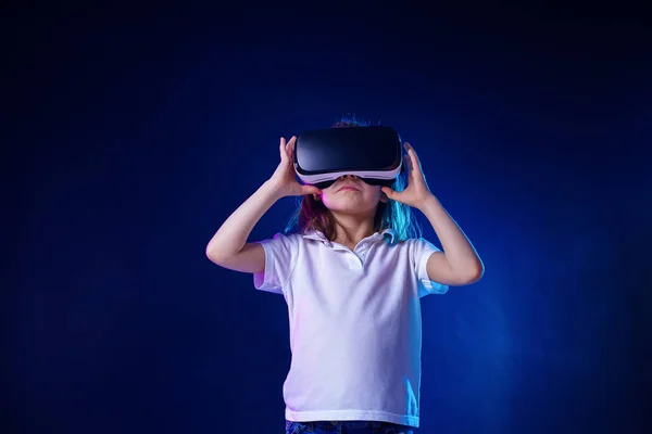 Menina 7 anos. experimentando jogo de fone de ouvido VR em fundo colorido. Criança usando um gadget de jogo para realidade virtual . — Fotografia de Stock