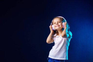 Kız koyu renkli arka plan üzerinde kulaklık müzik dinlerken . Dans eden kız. Mutlu küçük kız müzikle dans ediyor. Sevimli çocuk mutlu dans müziği zevk.