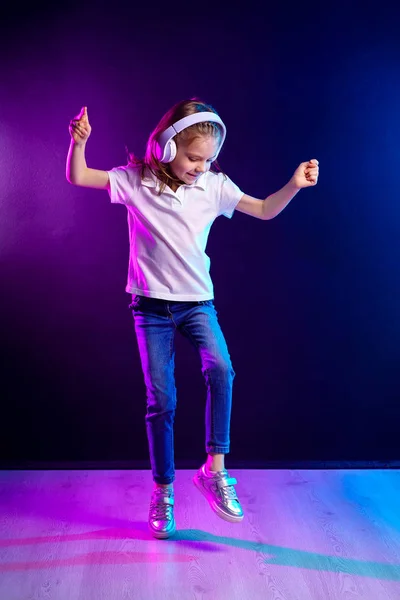 Lány hallgató-hoz zene-ban fejhallgató-ra sötét színdús háttér. Táncoló lány. Boldog kis lány táncol a zenére. Aranyos gyerek élvezi boldog tánczene. — Stock Fotó